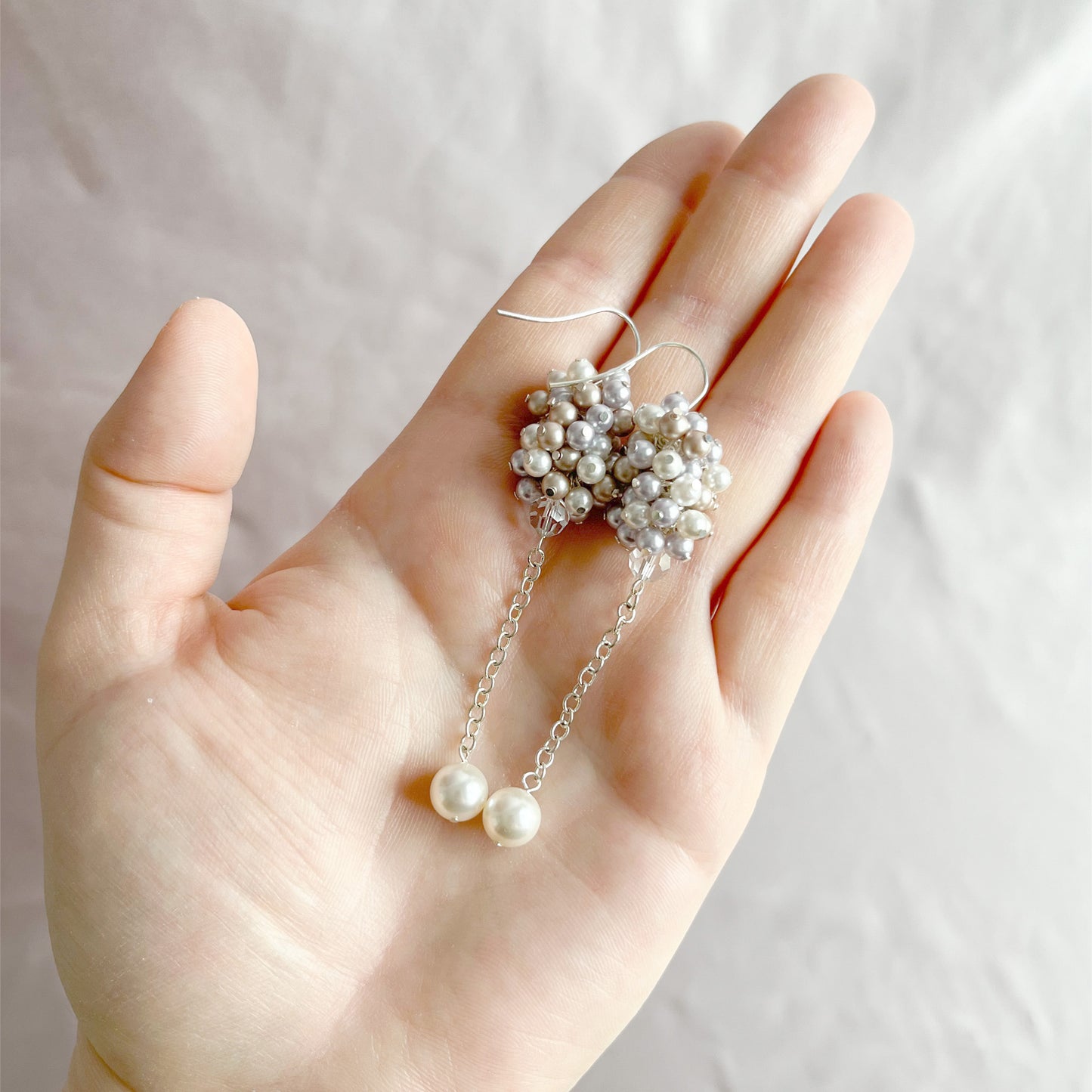 Lavender and almond pearl earrings resting on an open hand, shown for size and romantic texture.