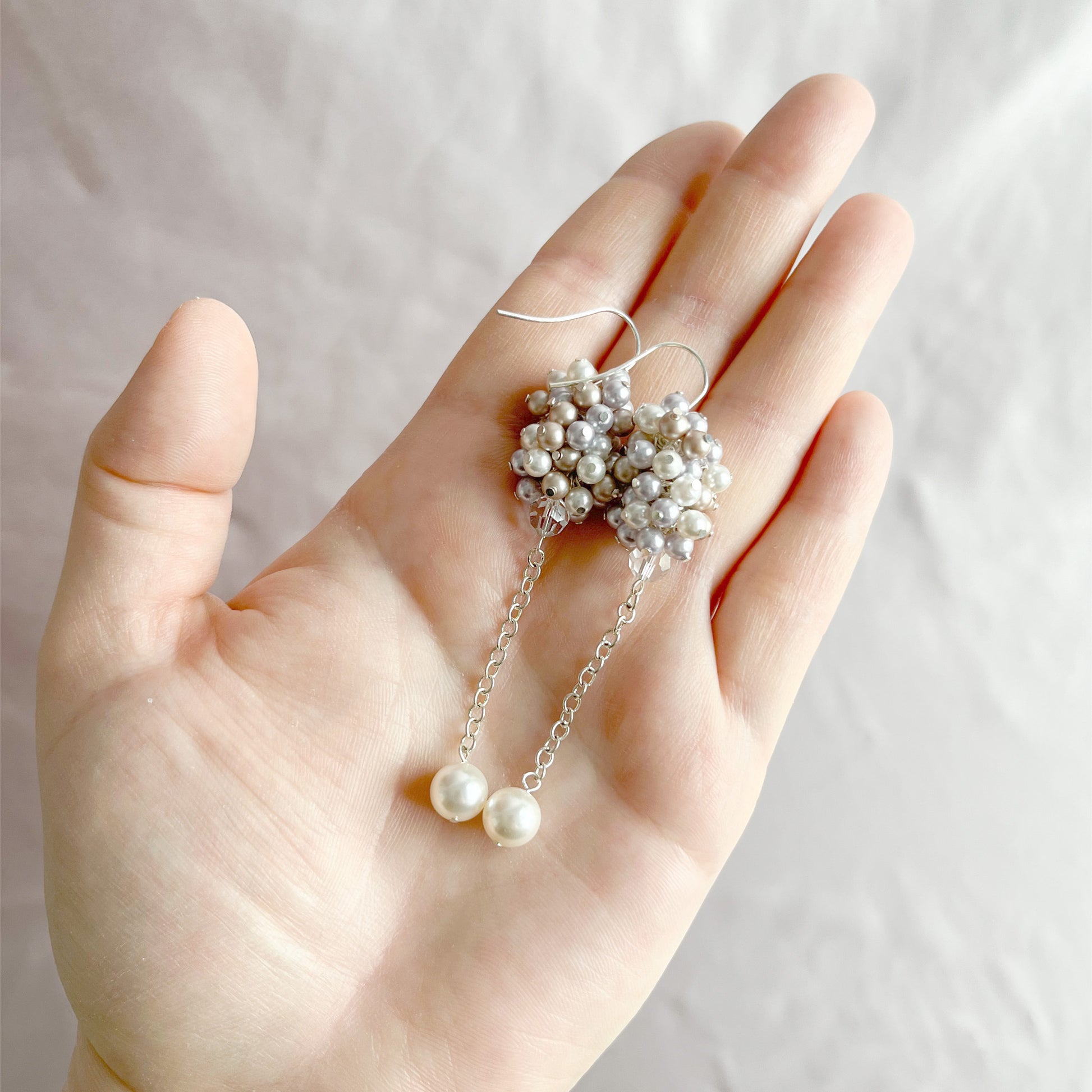Lavender and almond pearl earrings resting on an open hand, shown for size and romantic texture.