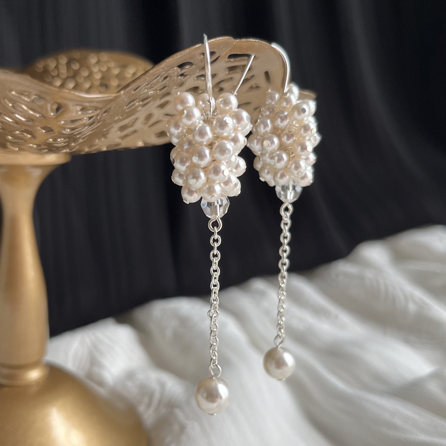 White pearl cluster earrings in side view close-up on brass earring stand, bridal style with romantic detail.