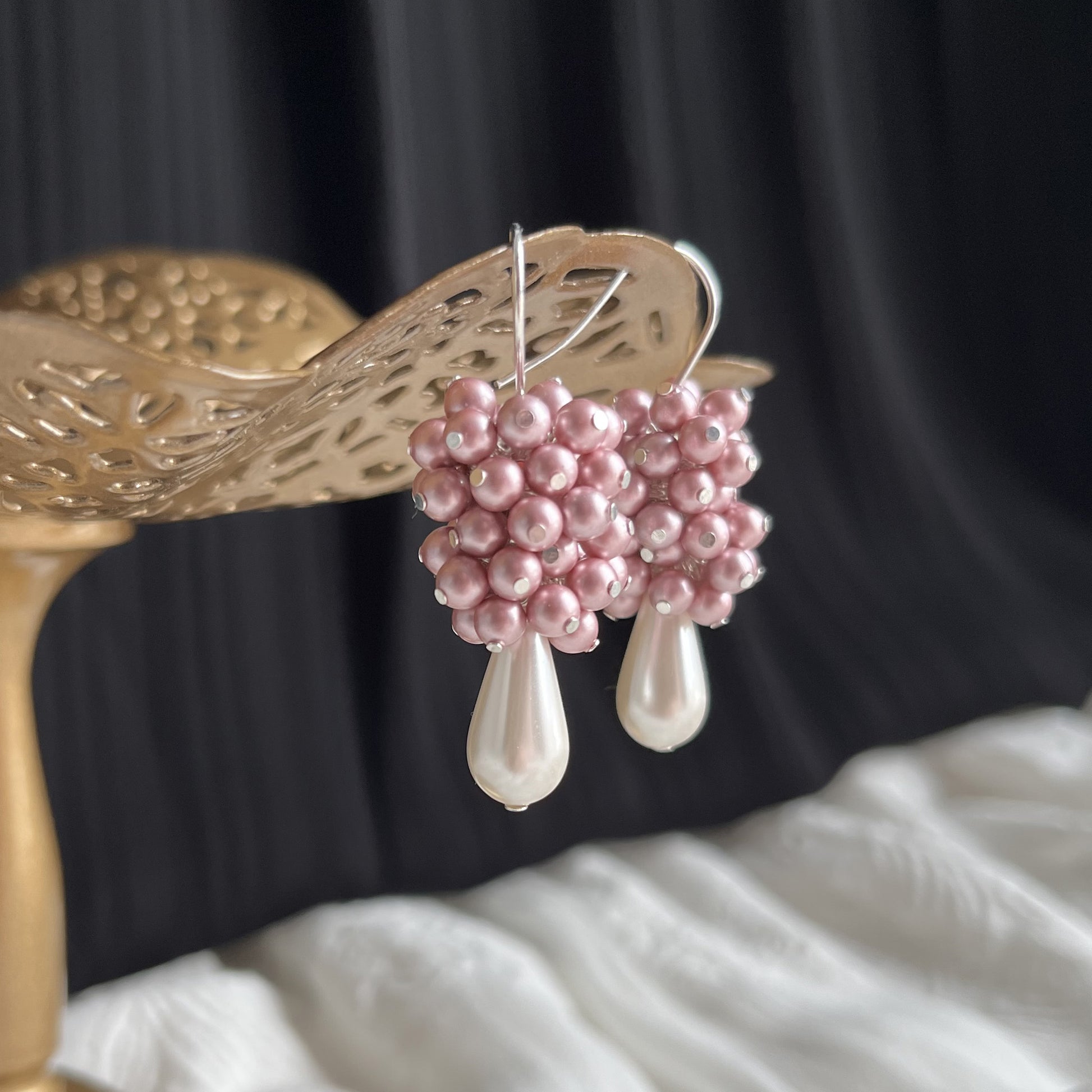 Side view close-up of pink pearl cluster earrings on a brass earring stand, highlighting soft luster and shape.