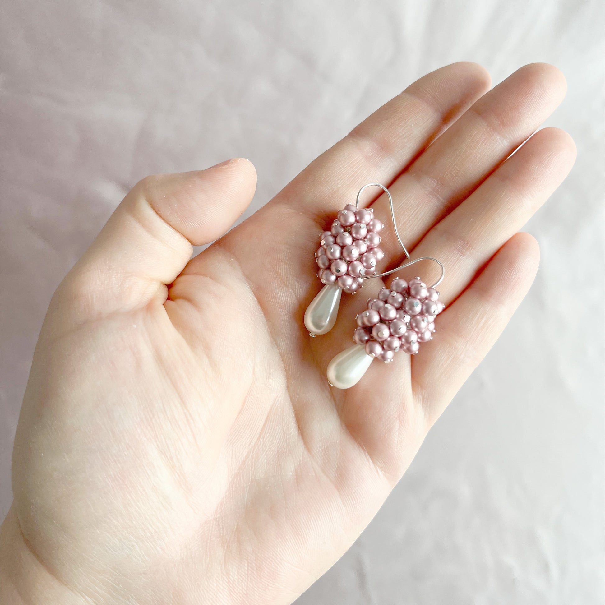 Pink pearl cluster earrings resting on an open hand, shown for scale and romantic texture.