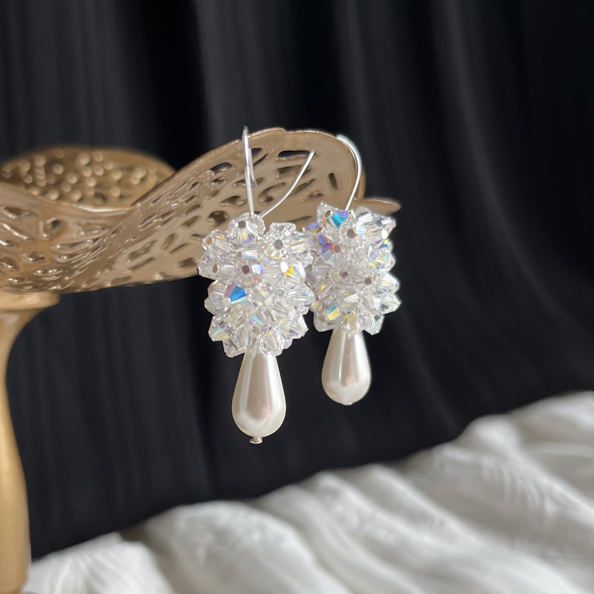 Detailed side-angle view of white pearl and crystal cluster earrings on brass stand, romantic and luminous.