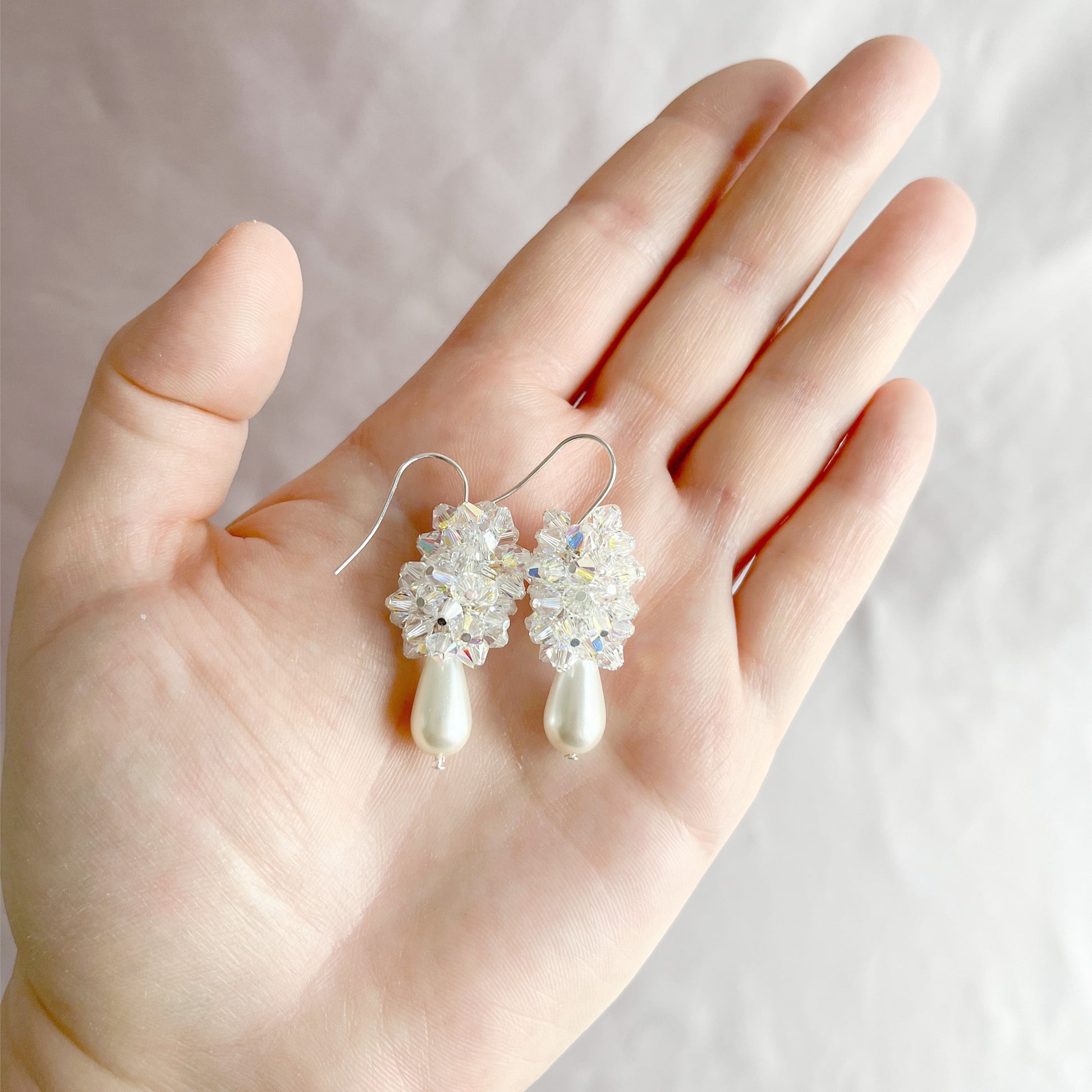White pearl and crystal cluster earrings on an open hand, highlighting their size and elegant design.