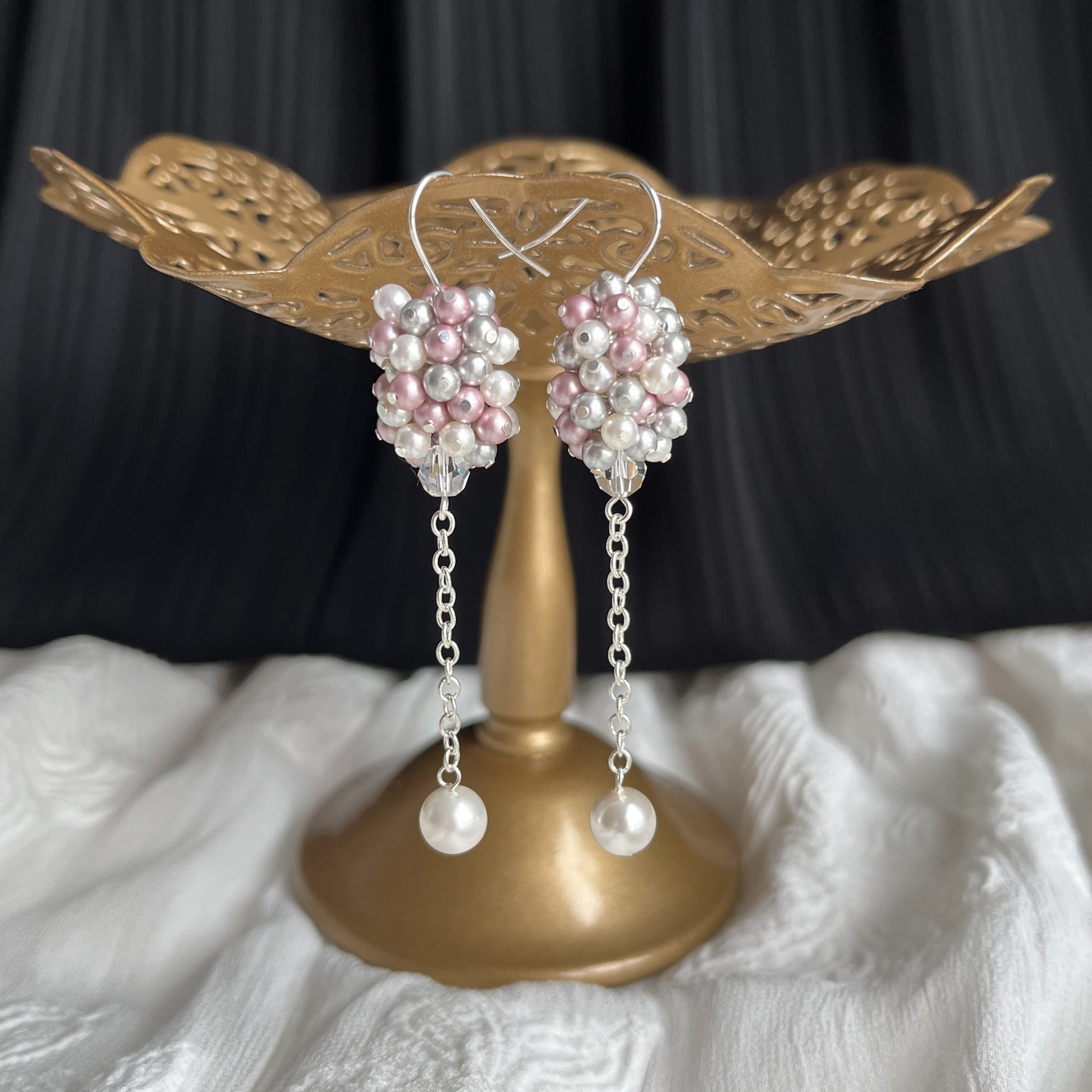 Pink and gray pearl cluster earrings displayed on a brass earring stand, handcrafted and subtly colorful.