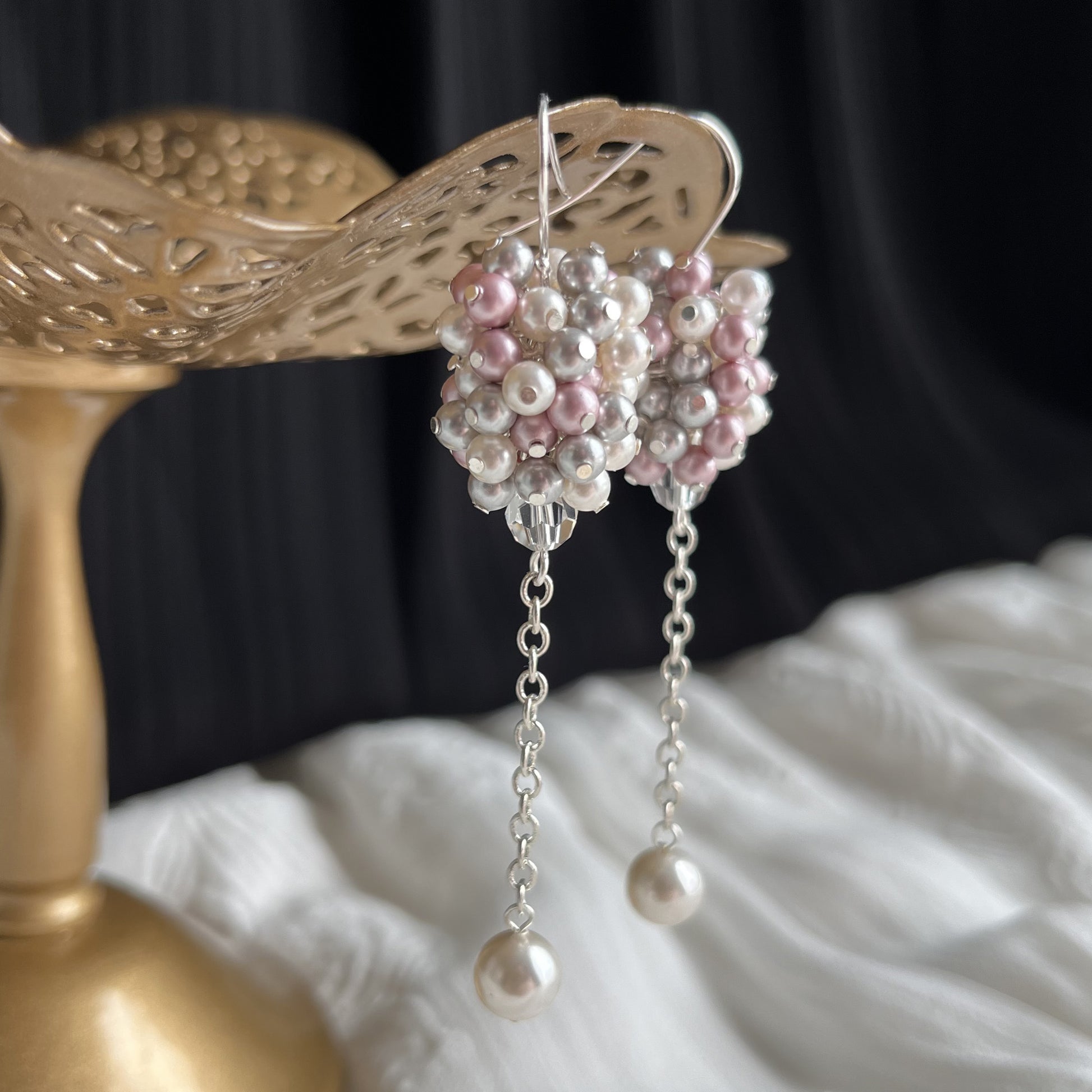 Side-angle detail of pink and gray pearl cluster earrings on brass stand, with handcrafted texture.