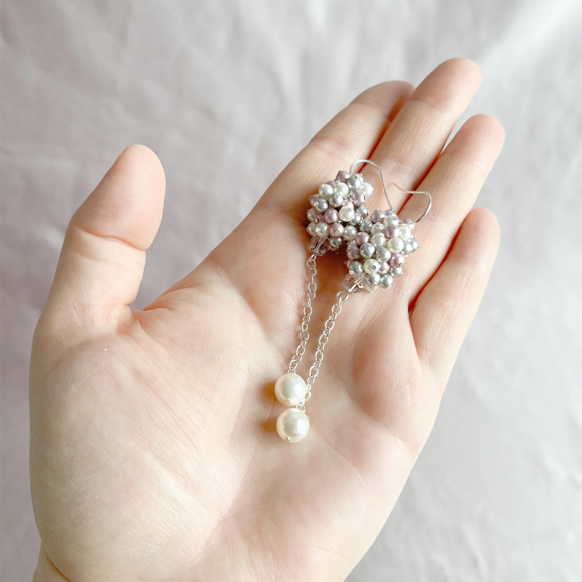 Pink and gray pearl earrings on an open hand, showing scale and handcrafted pearl detail.