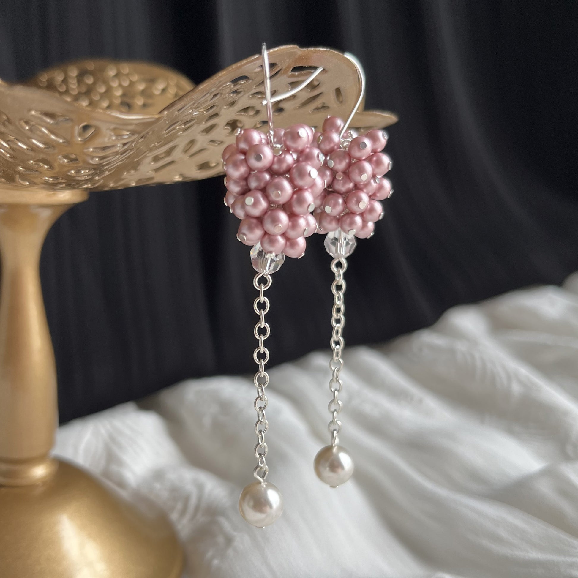 Close-up of pink pearl cluster earrings on brass stand from side angle, showing delicate handcrafting.
