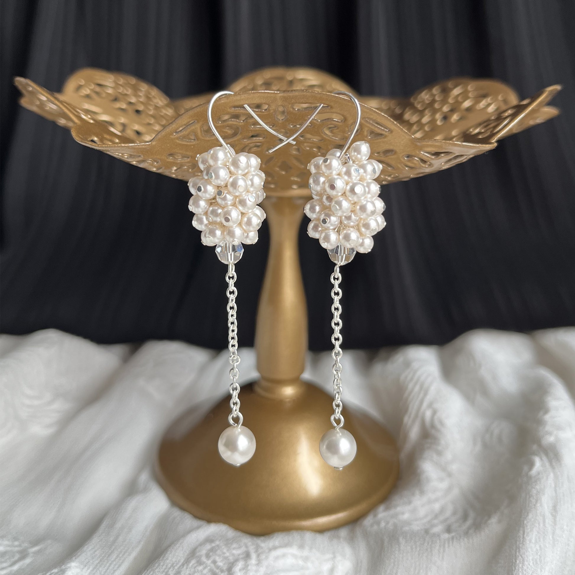 White pearl cluster dangle earrings displayed on a brass stand, handcrafted with timeless bridal charm.