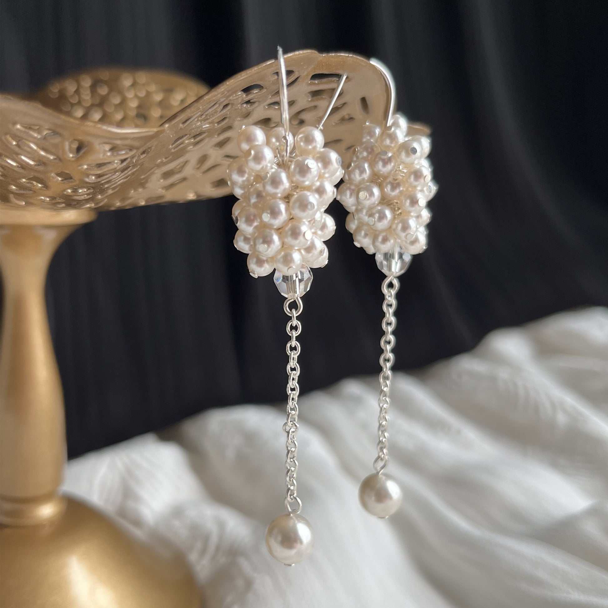 White pearl cluster earrings in side view close-up on brass earring stand, bridal style with romantic detail.