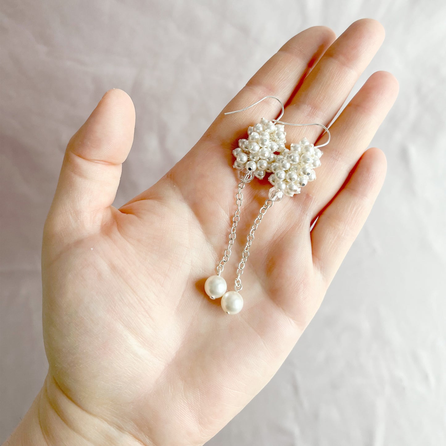 White pearl cluster earrings displayed on an open hand to show scale and bridal craftsmanship.
