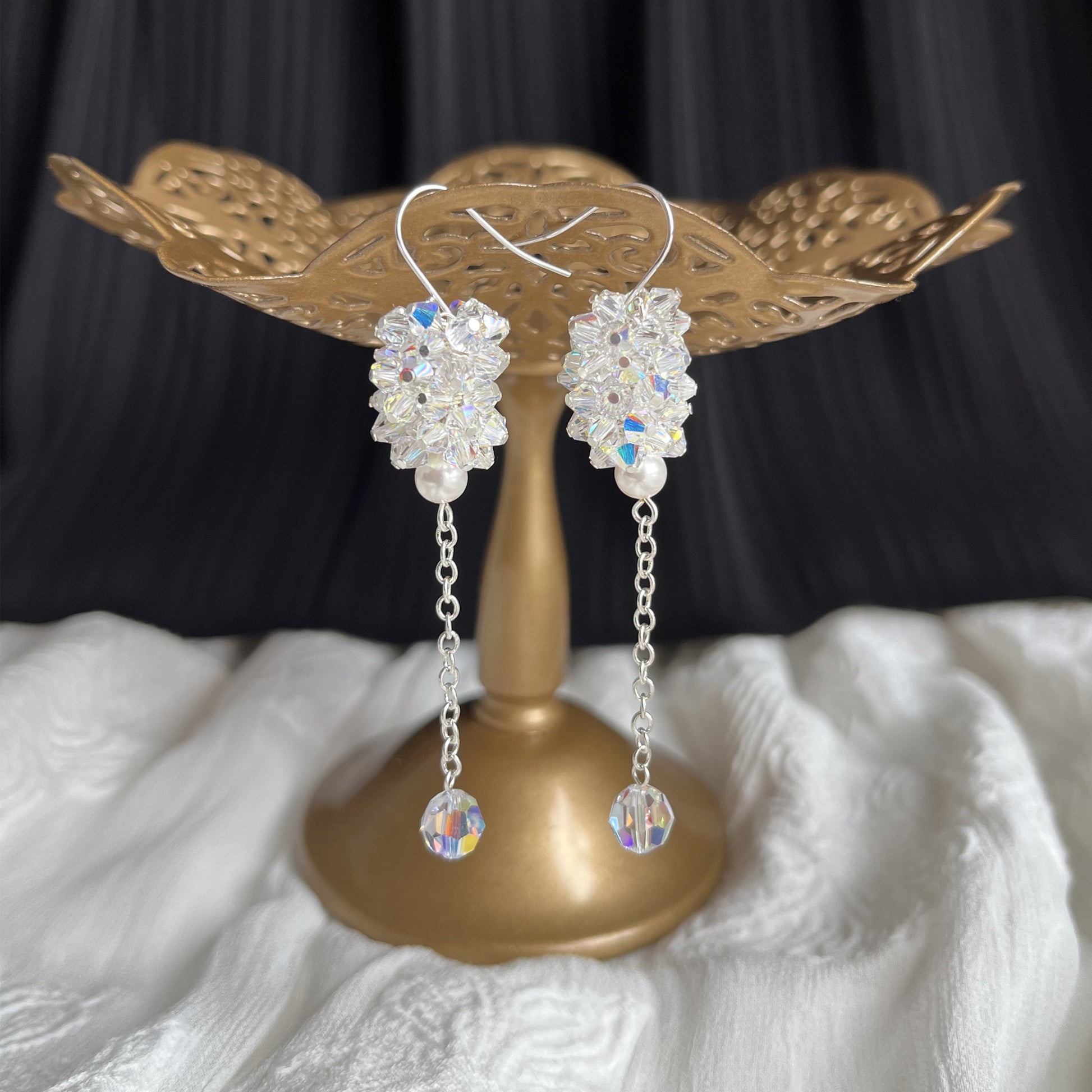 Clear crystal and pearl dangle earrings displayed on a brass stand, sparkling and elegant for bridal wear.