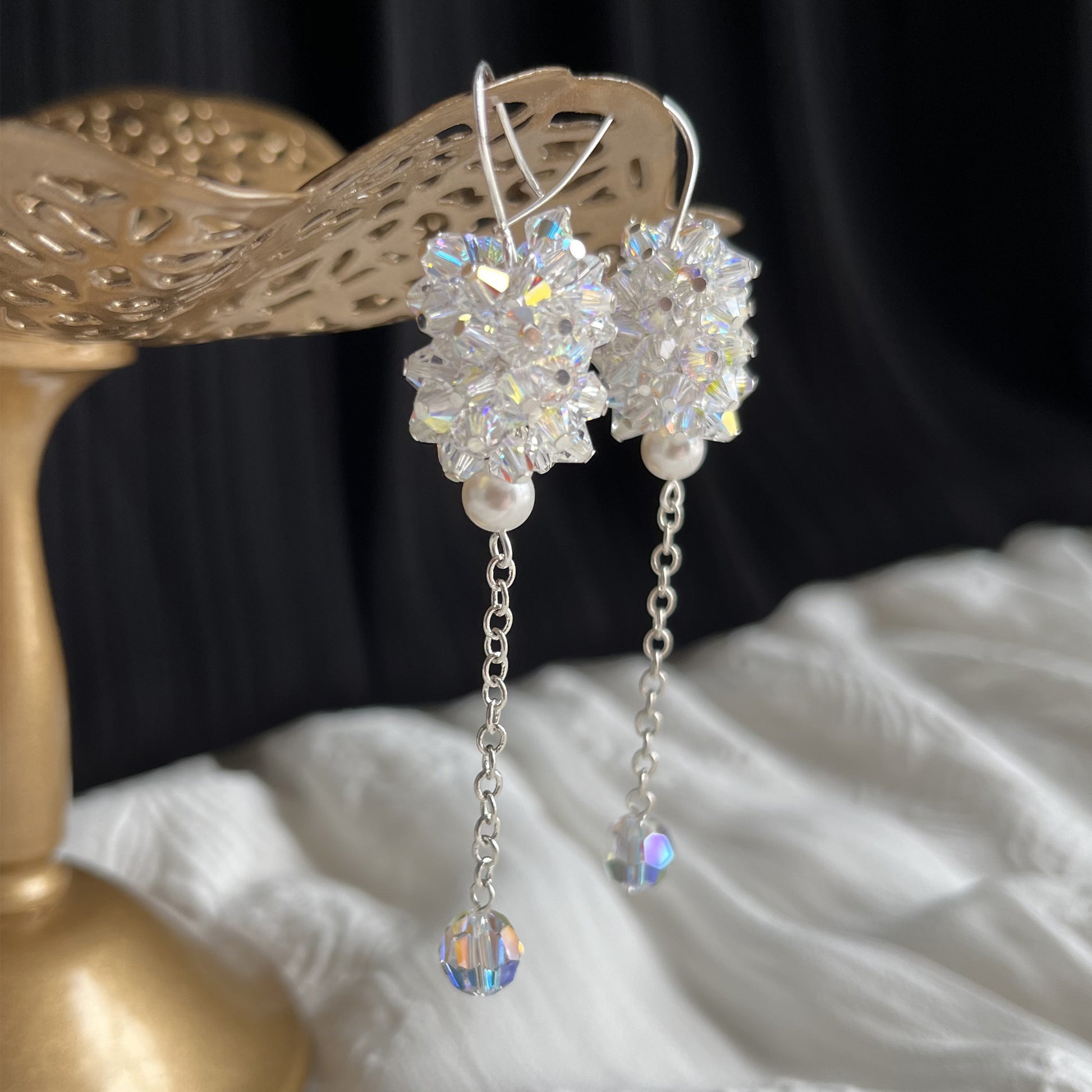 Clear crystal and pearl earrings in close-up side angle on brass earring stand, radiant and elegant.