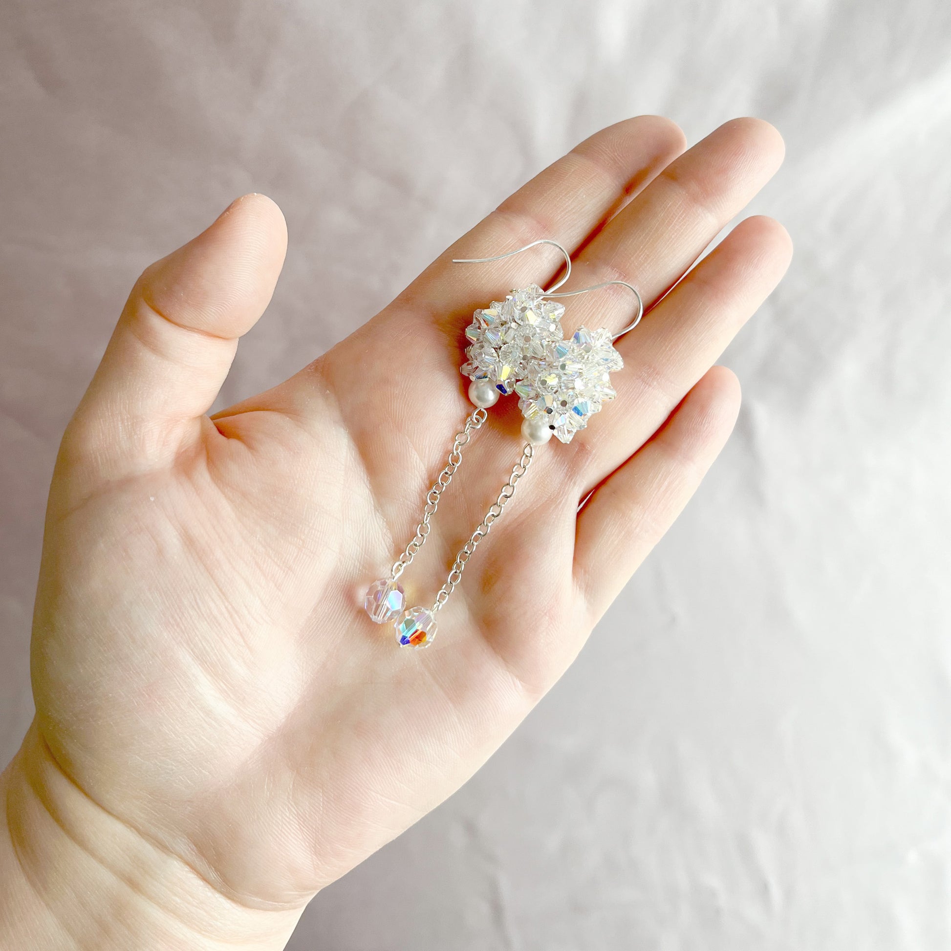 Clear crystal and pearl earrings displayed on an open hand to show size and radiant sparkle.