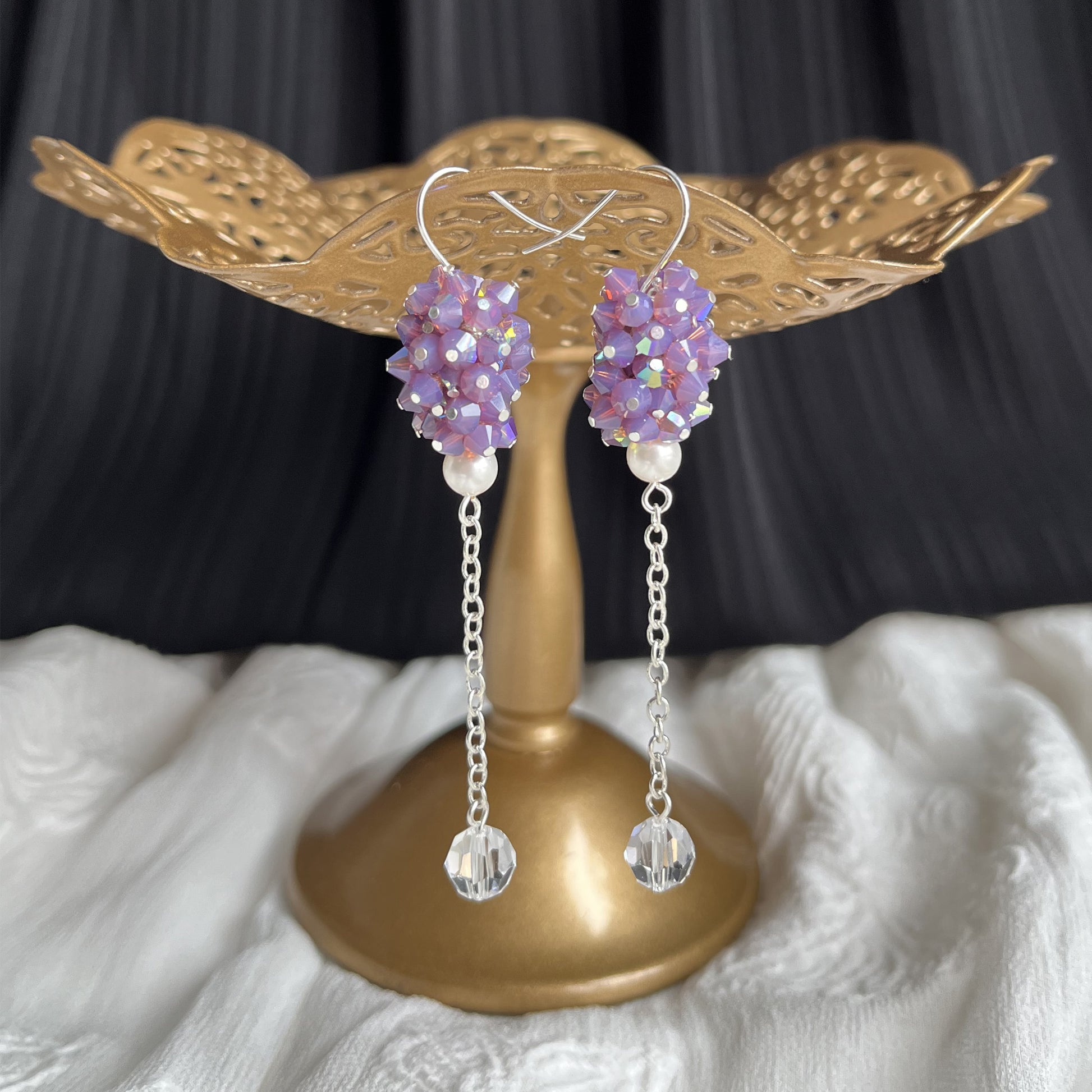 Purple crystal and pearl dangle earrings on a brass earring stand, delicate and luminous.