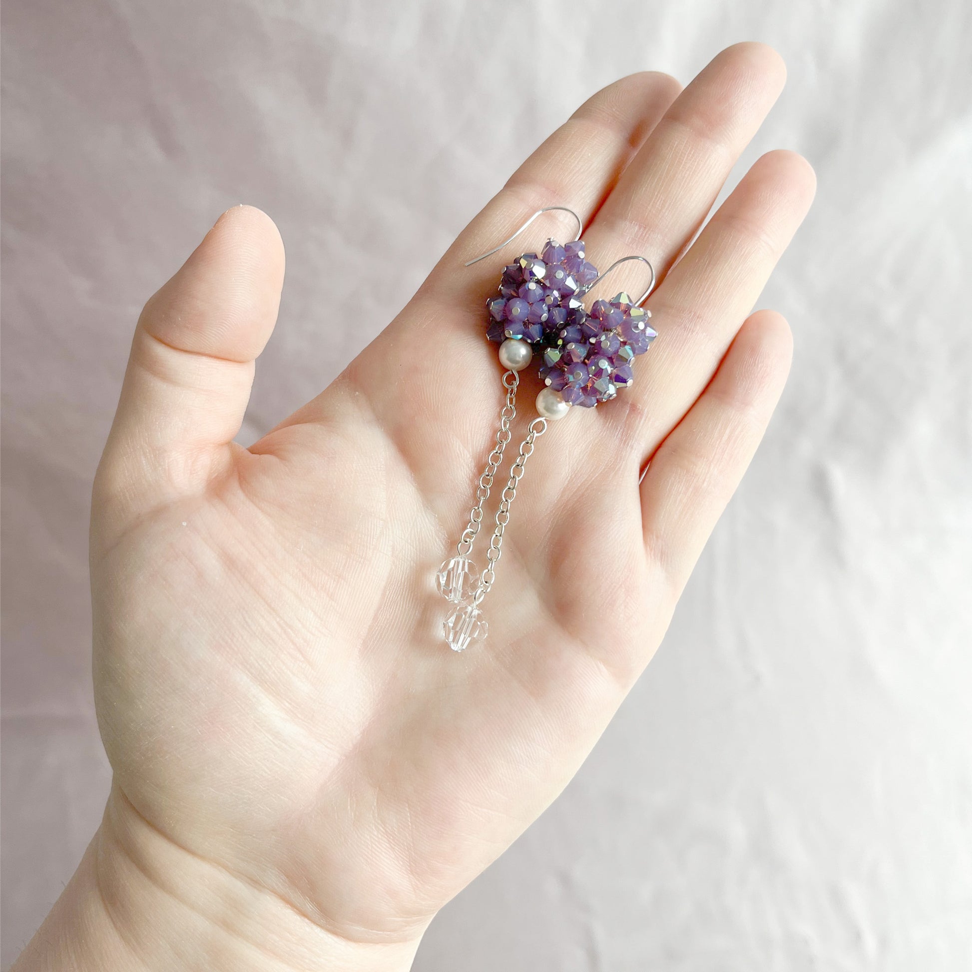 Purple crystal and pearl earrings on an open hand, highlighting size and shimmering texture.