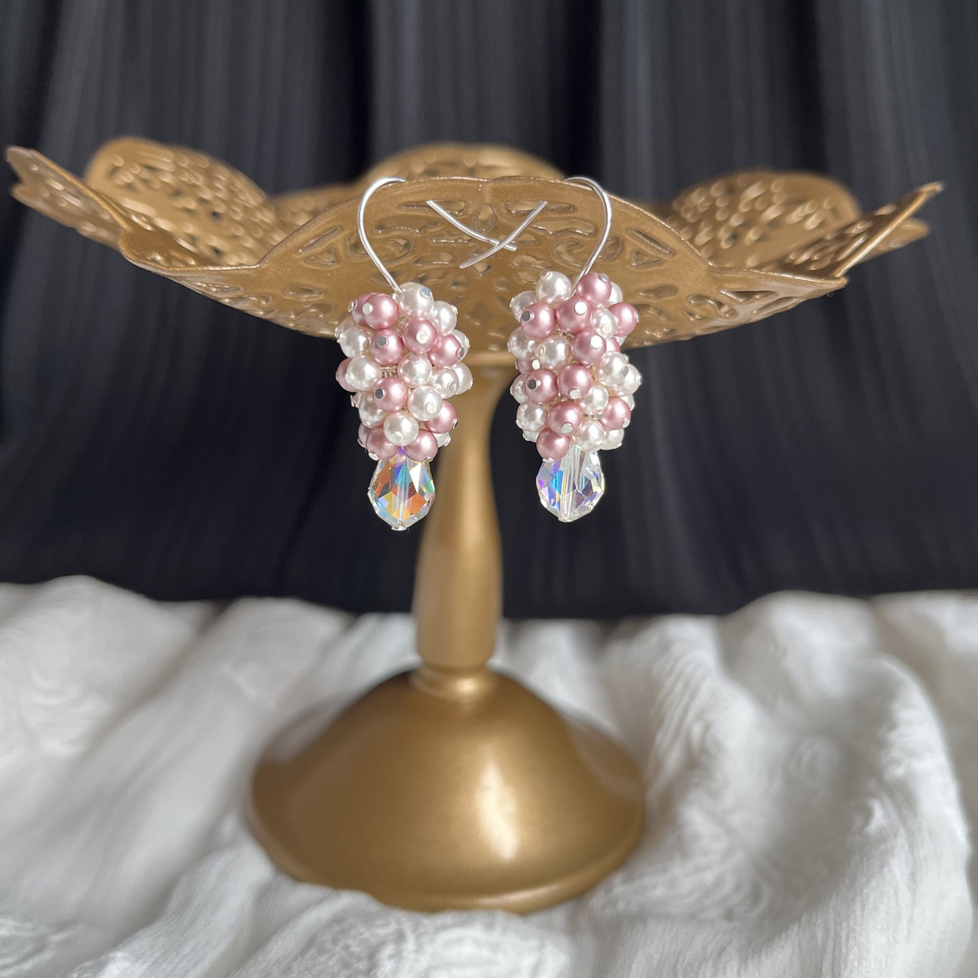 Blush and white pearl and crystal earrings displayed on a brass earring stand, romantic and shimmering.