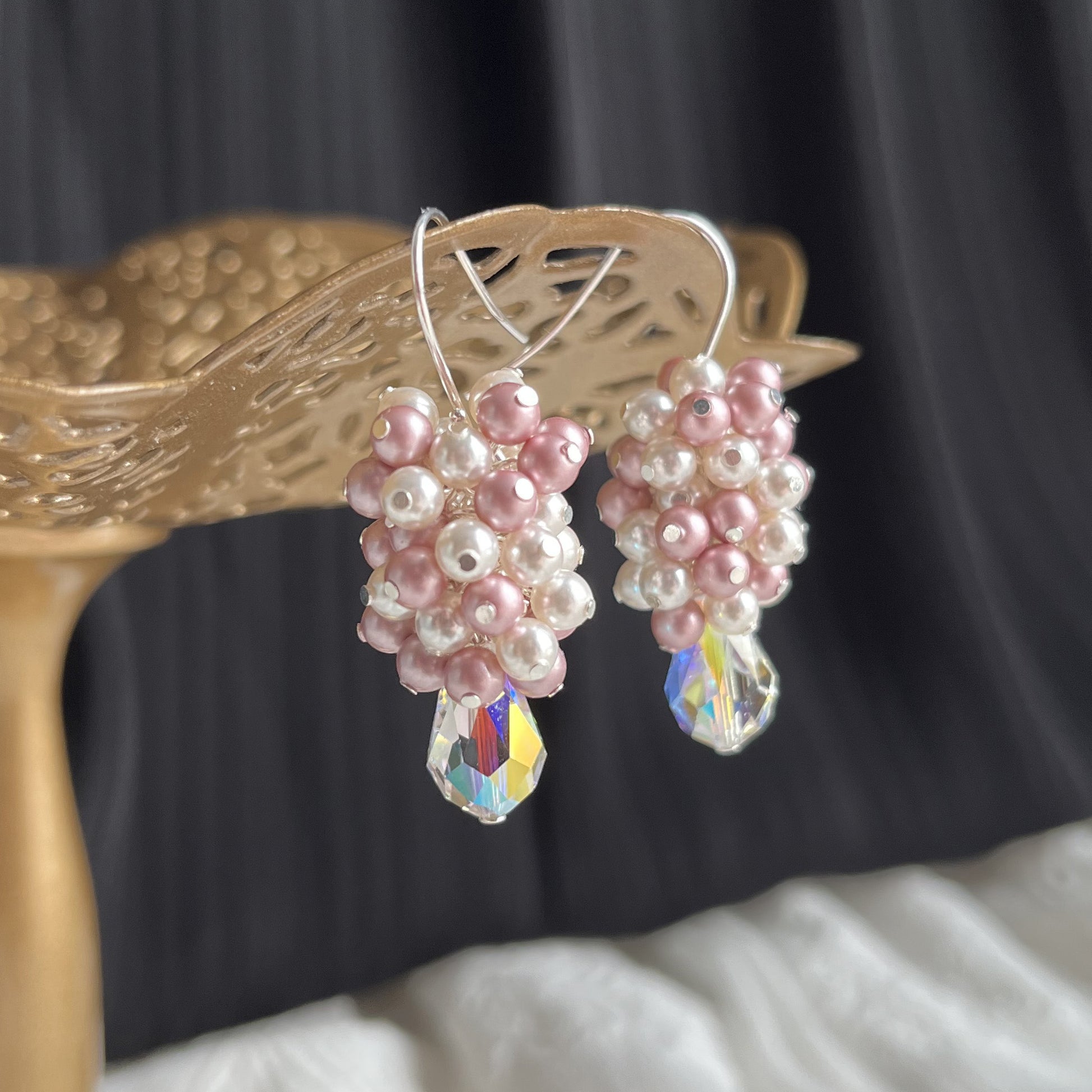 Close-up of pink and white pearl and crystal cluster earrings on brass stand, showing texture and sparkle.