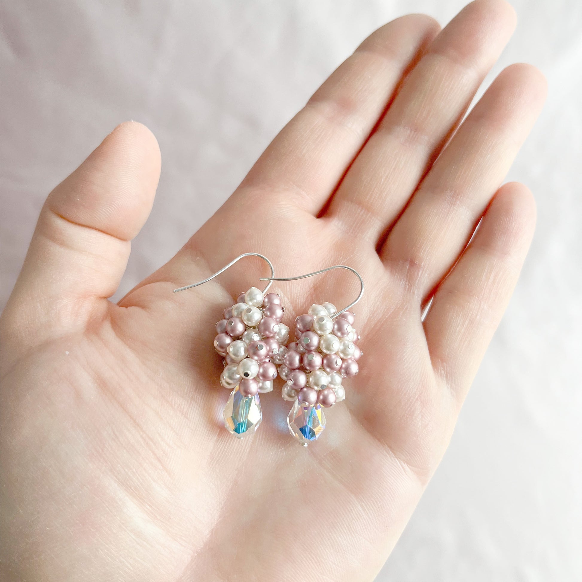 Pink and white pearl and crystal earrings displayed on an open hand for scale and sparkle.