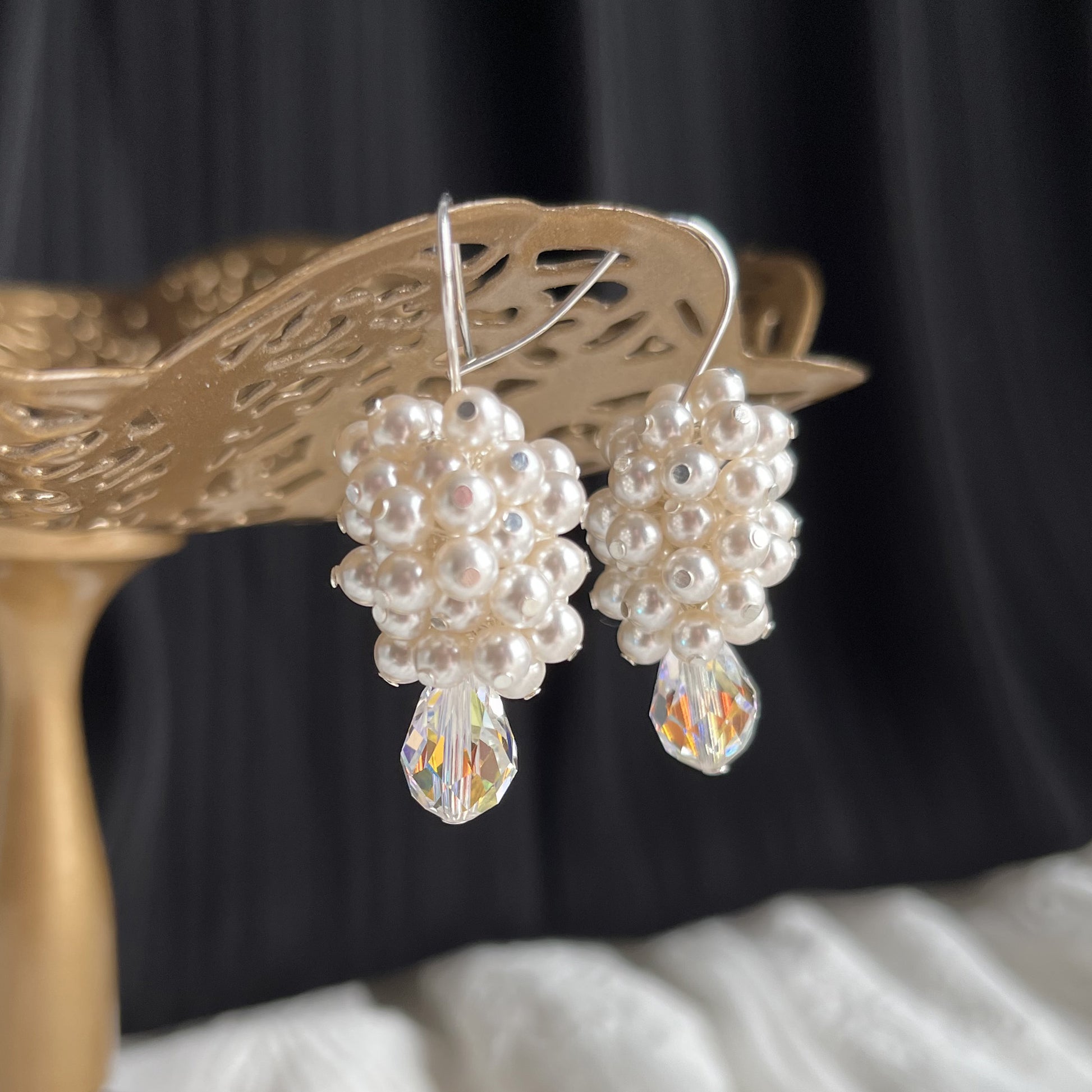 Side-angle close-up of white pearl and crystal earrings on a brass stand, crafted with bridal elegance.