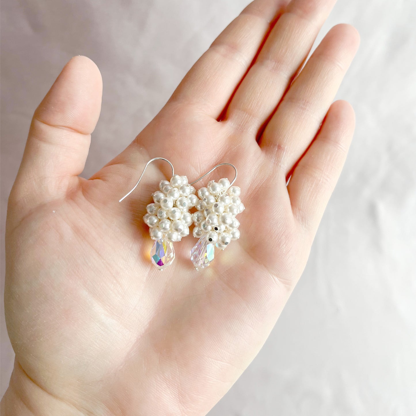 White pearl and crystal bridal earrings resting on an open hand to show their size and delicate design.