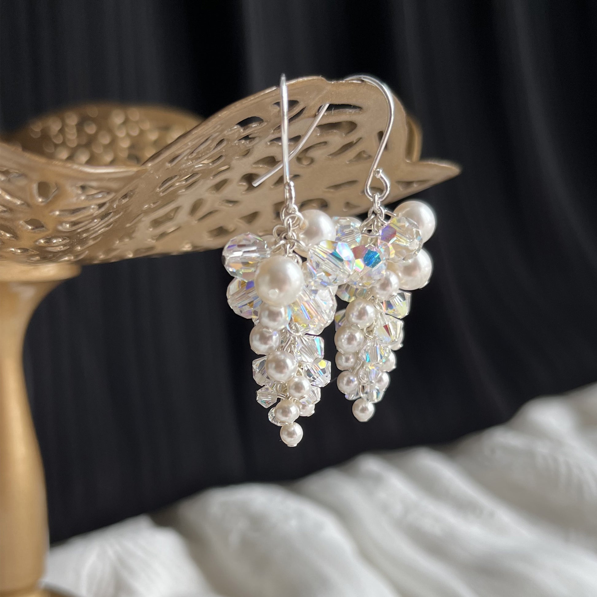 Close-up side view of white pearl and crystal dangle earrings on a brass stand, showcasing handcrafted detail.