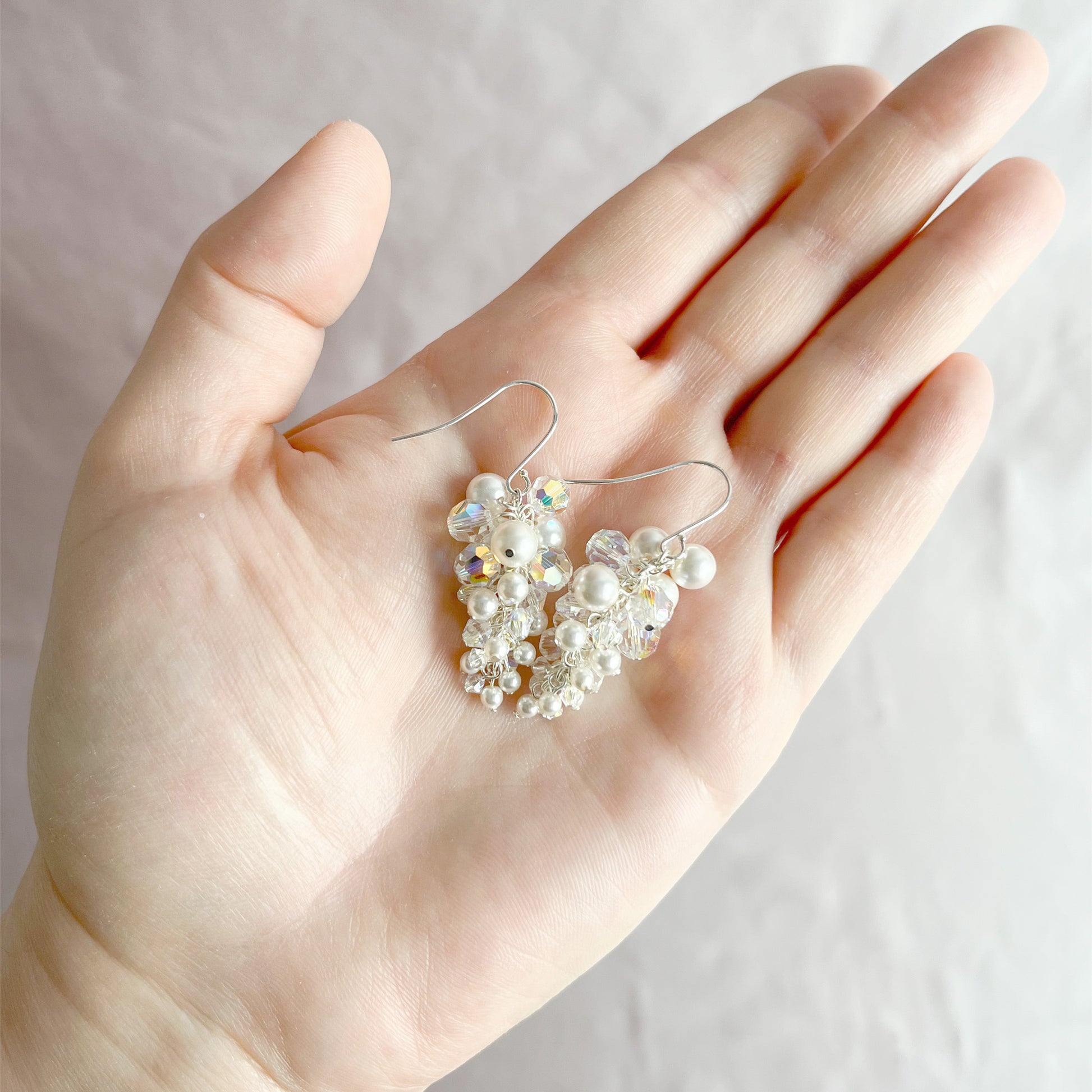 White pearl and crystal dangle earrings displayed on an open hand to show size and handcrafted detail.